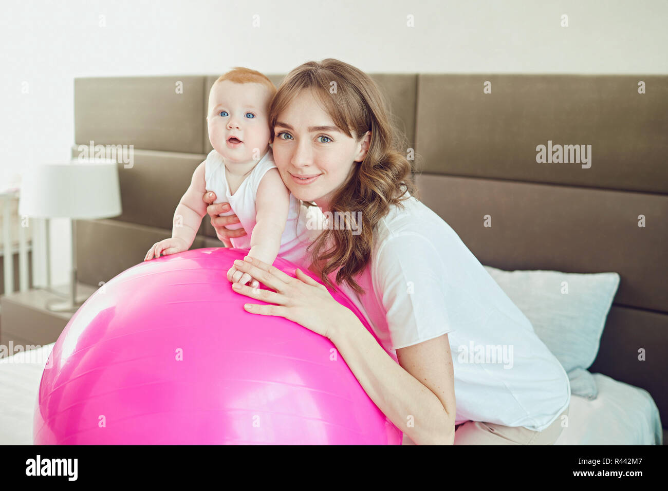 Mère avec le bébé sur la balle Pilates sur le lit. Banque D'Images