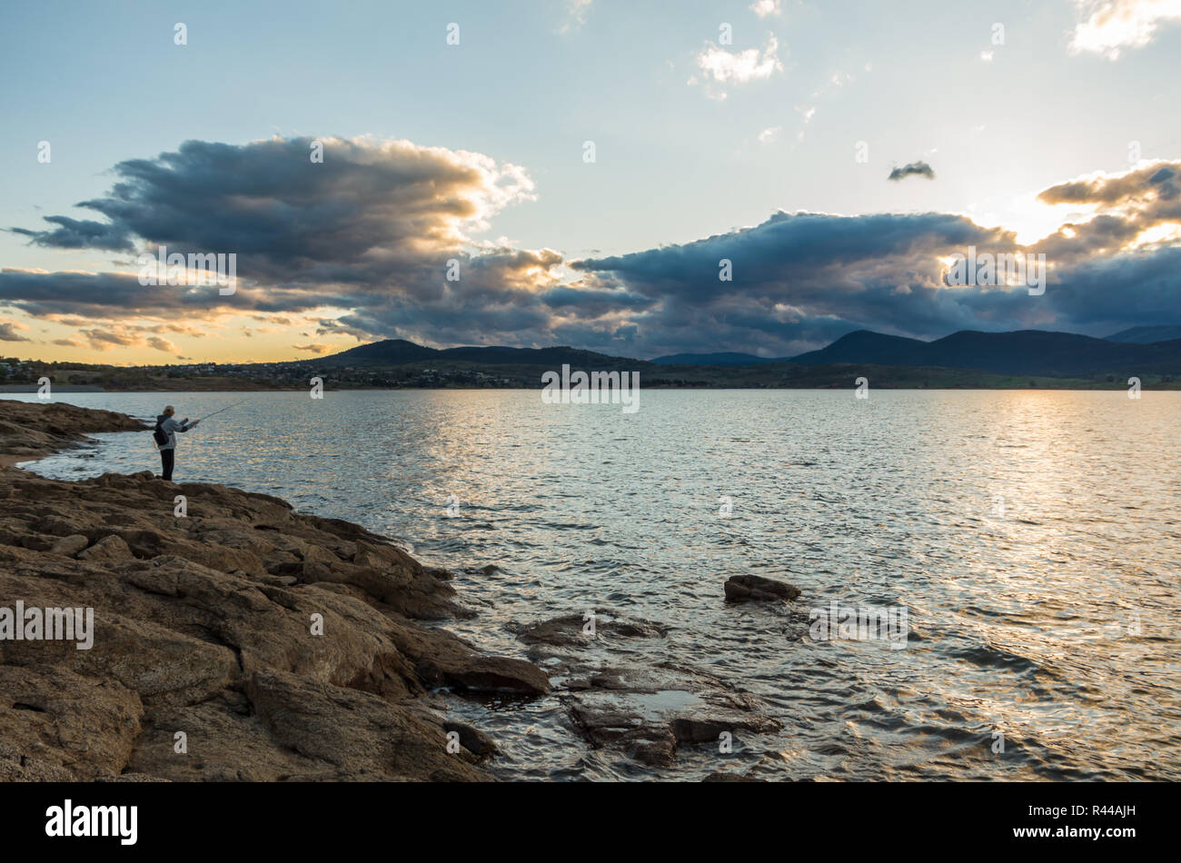 Au bord d'un pêcheur au coucher du soleil à Jindabyne dans l'arrière-plan Banque D'Images