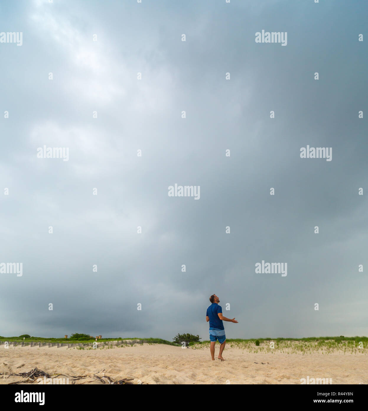 Image d'un homme adulte à la recherche jusqu'à un ciel d'orage en étant debout sur une plage dans l'Est de Long Island, NY Banque D'Images