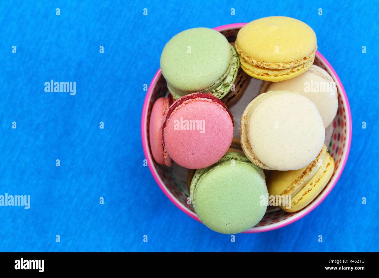 Macarons colorés dans un bol bleu vif sur surface avec copie espace Banque D'Images