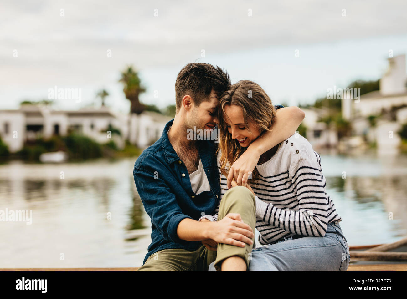 Jeune homme et femme dans une humeur romantique assis près d'un lac. Jeune homme assis avec sa petite amie près d'un lac avec son bras autour de son cou. Banque D'Images