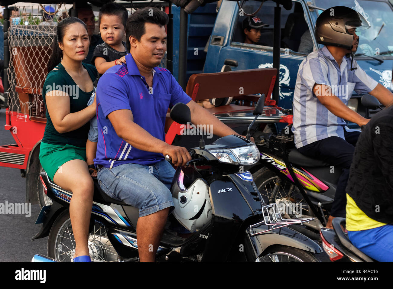 Couple avec enfant le scooter dans le trafic important sur le bord de la rivière au coucher du soleil. Preah Sisowath Quay, centre-ville, Phnom Penh, Cambodge Banque D'Images