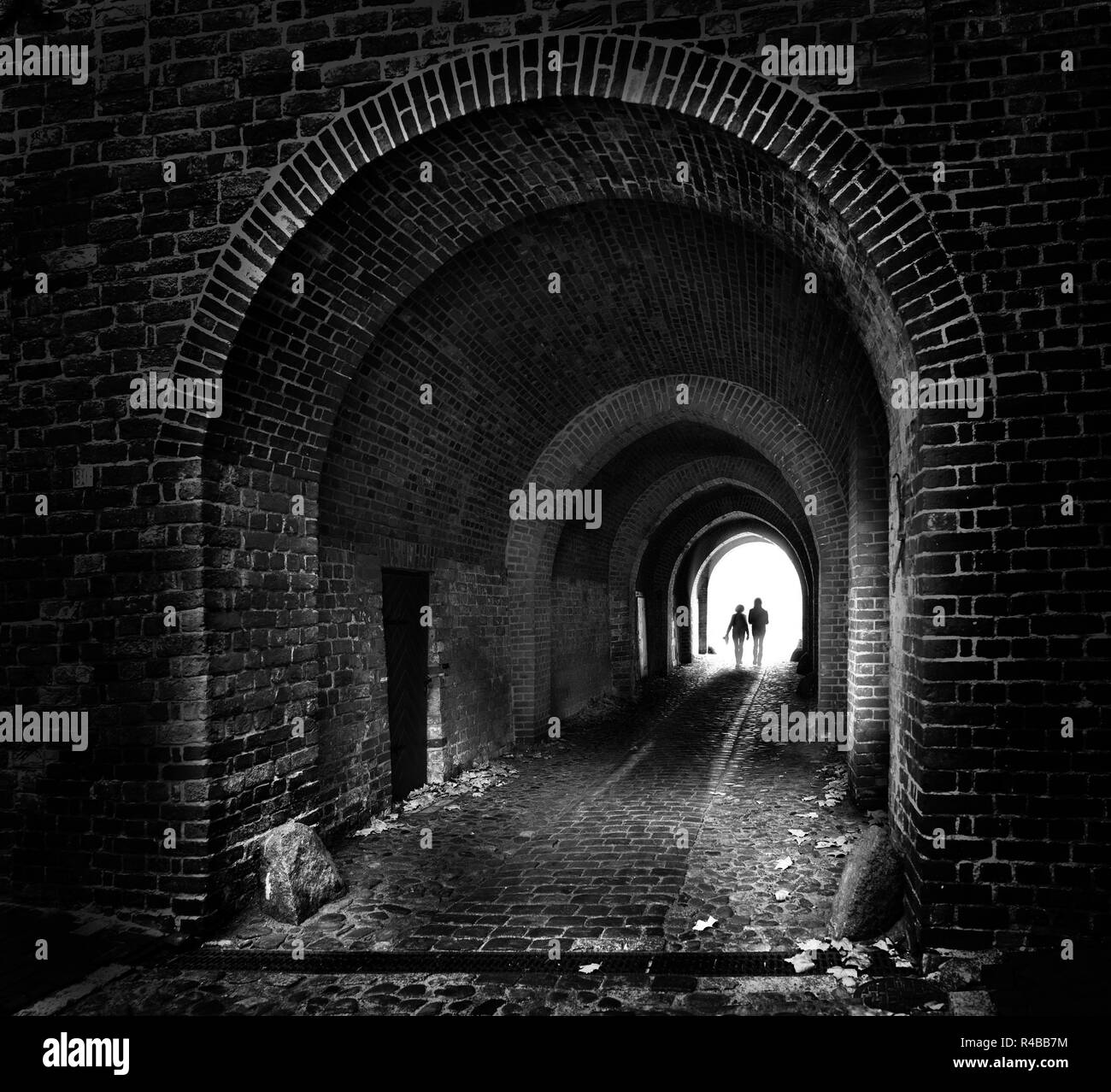 Deux silhouettes sont les gens à marcher ensemble comme un couple dans un vieux tunnel en brique sombre à la lumière, concept futur en noir et blanc Banque D'Images