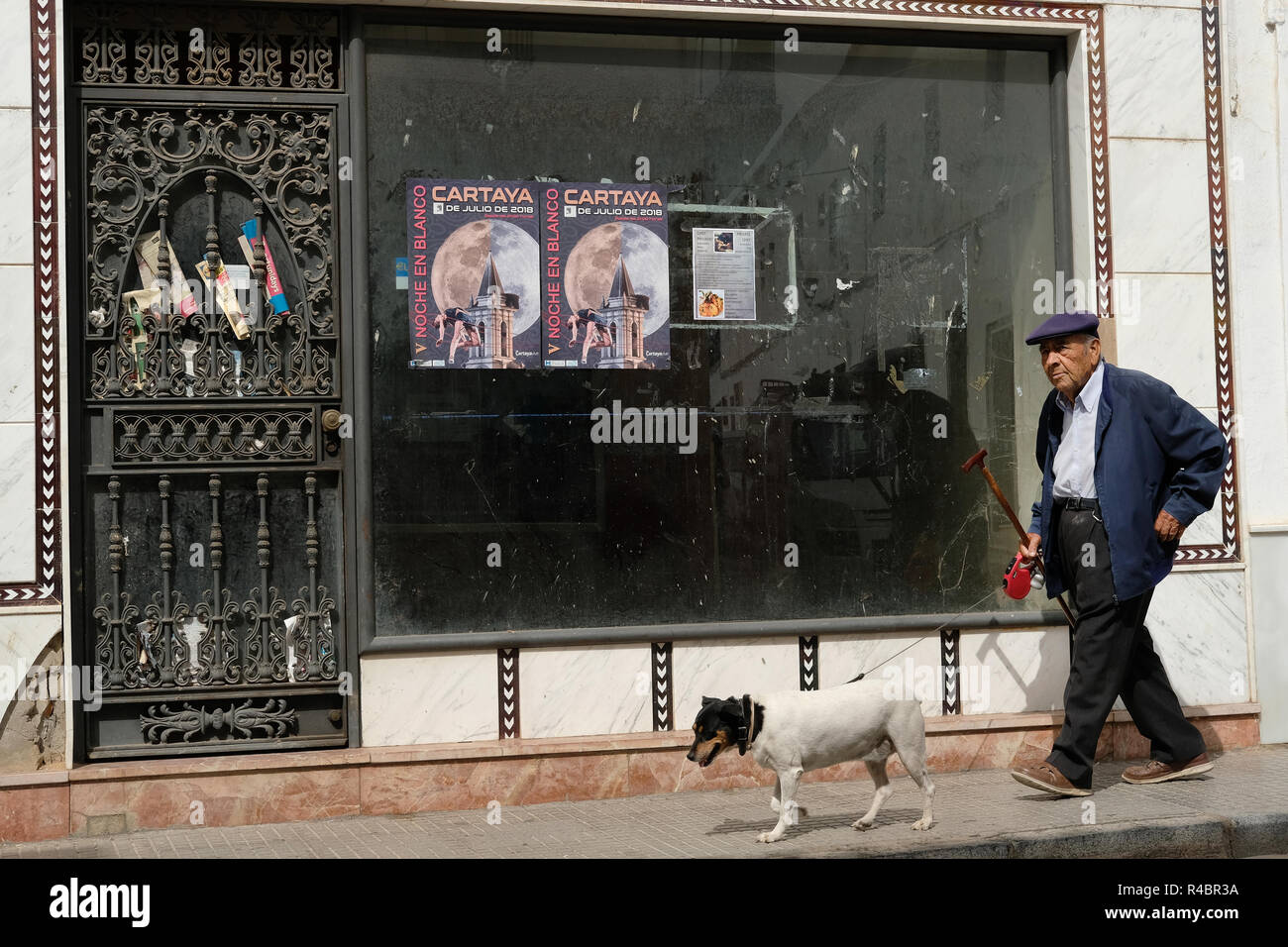 Un vieil homme espagnol promenait son chien au-delà d'un magasin qui est fermé. Banque D'Images