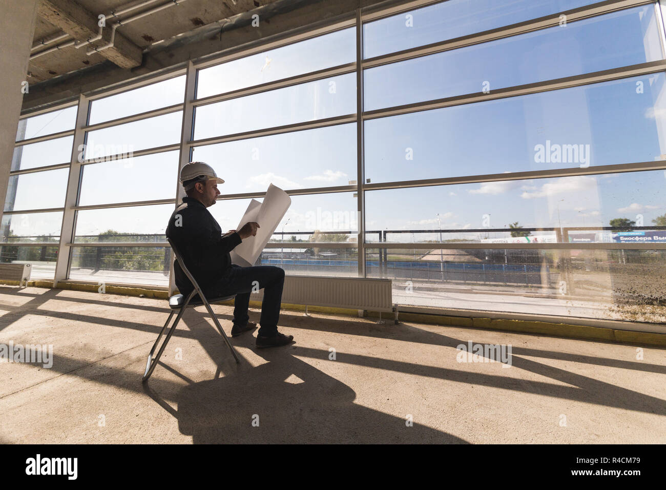 Le constructeur architecte dans un casque avec dessins travaille sur le chantier de construction. la supervision de la construction. Banque D'Images