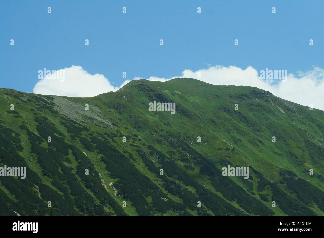 Une vue panoramique d'un Grassy Mountain Ridge contre le ciel avec les nuages qui de derrière la crête de la montagne. Banque D'Images