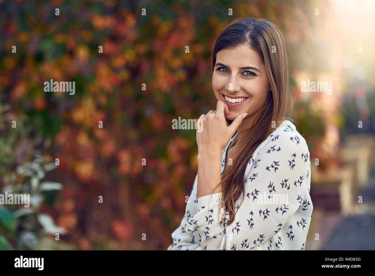 Belle jeune femme dans une rue ou l'automne automne coloré debout sur le côté pour l'appareil photo avec sa main sur sa joue en souriant à l'appareil photo Banque D'Images