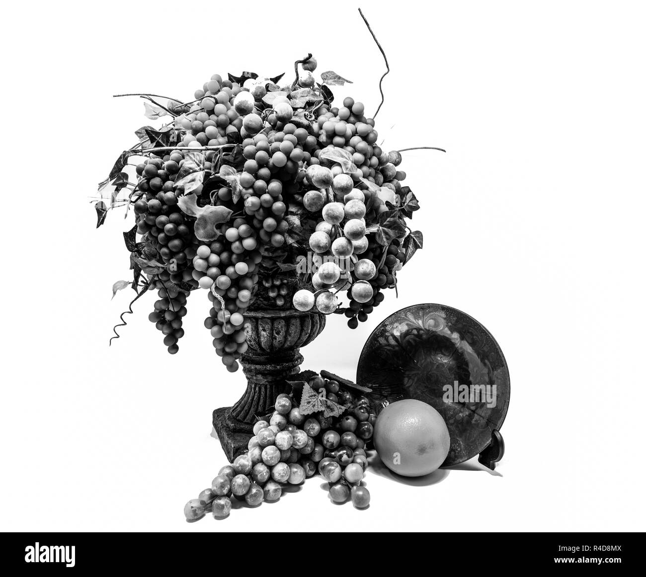 Noir et blanc à contraste élevé de la vie toujours des raisins dans un vase en face d'une orange et une plaque de verre. Banque D'Images