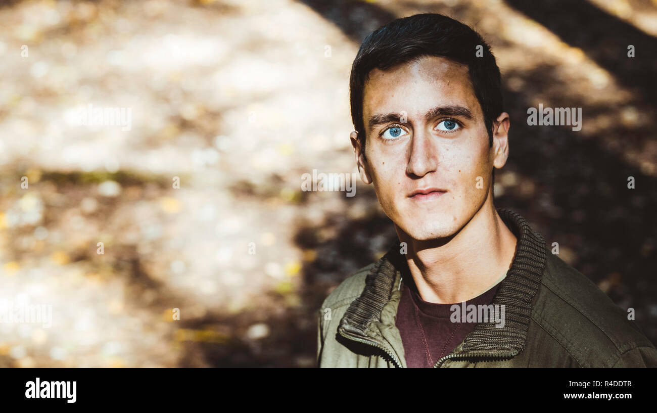 Beau jeune homme avec de beaux yeux bleus à l'avant, avec les bokeh de la nature de l'arrière-plan Banque D'Images