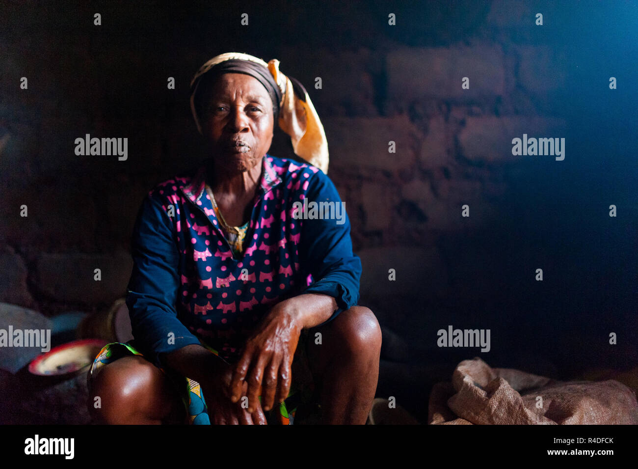 Bafoussam, Cameroun - 06 août 2018 : old african lady dans sa cuisine maison rurale avec un costume traditionnel le regardant dans Appareil photo avec confiance expr Banque D'Images