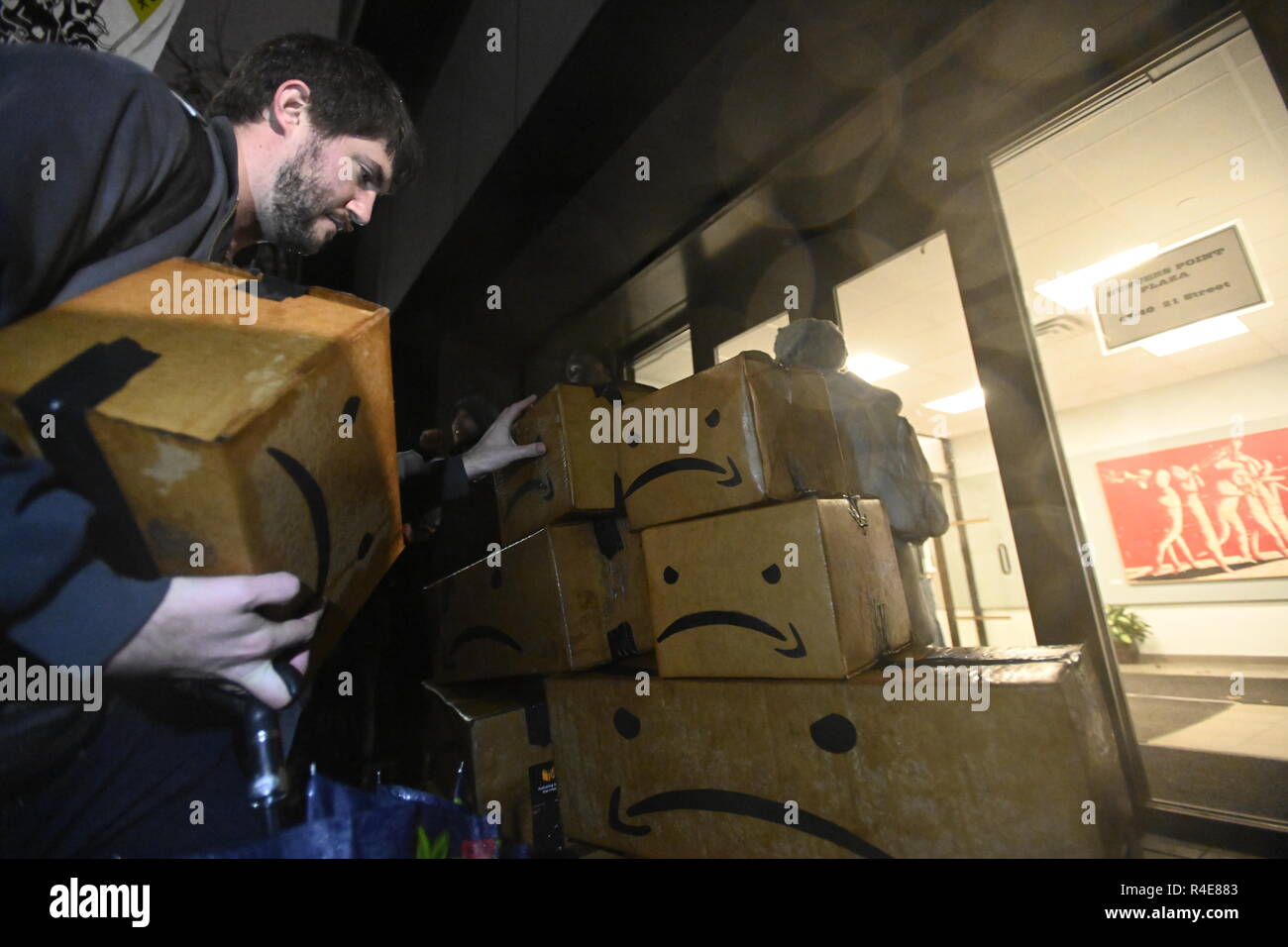 Queens, New York, USA. 26 Nov 2018 des pluies sur une cyber lundi, des manifestants qui protestaient contre le projet de construction d'un nouveau siège à Queens laissez les cases portant une version satirique de Amazon's logo à l'extérieur de l'immeuble de bureaux de l'Assemblée générale de l'État de New York femme Catherine Nolan, qui soutient le projet. Les objections des manifestants : 2,5 milliards de dollars en subventions de l'État de New York pour le projet et la peur qu'il va nuire à l'industrie existante et augmenter le coût du logement. Crédit : Joseph Reid/Alamy Live News Banque D'Images