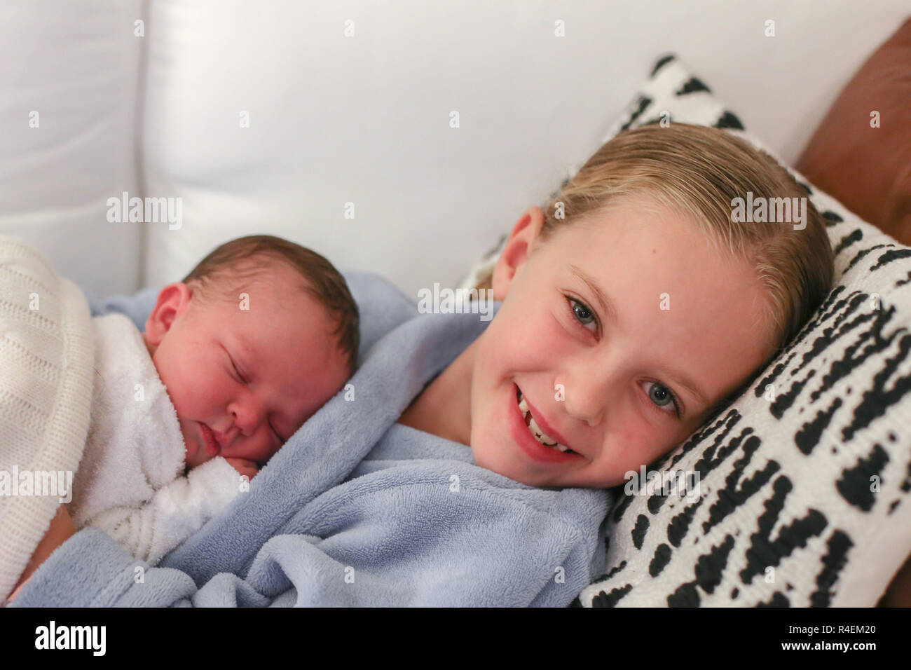 Smiling girl lying on couch with her baby sister Banque D'Images