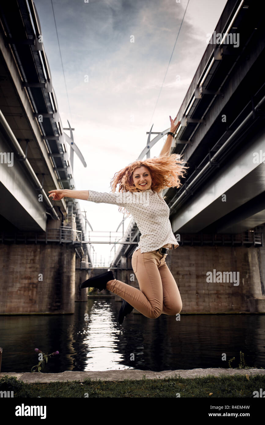 Femme sautant en l'air par une rivière, Belgique Banque D'Images