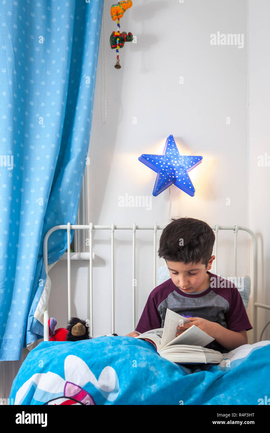 Garçon, âgé de 6 ans, lire un livre au lit Banque D'Images