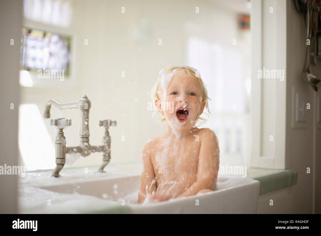 Portrait d'un enfant s'amusant rire tout en prenant un bain moussant. Banque D'Images