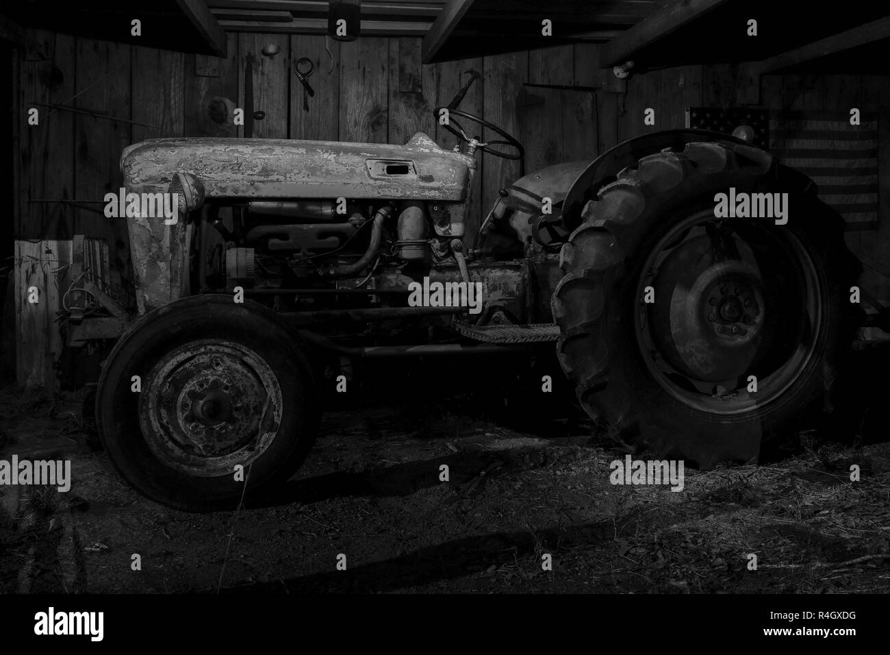 Le noir et blanc d'un vintage ou antique tracteur dans une vieille grange avec un drapeau américain en arrière-plan. Banque D'Images