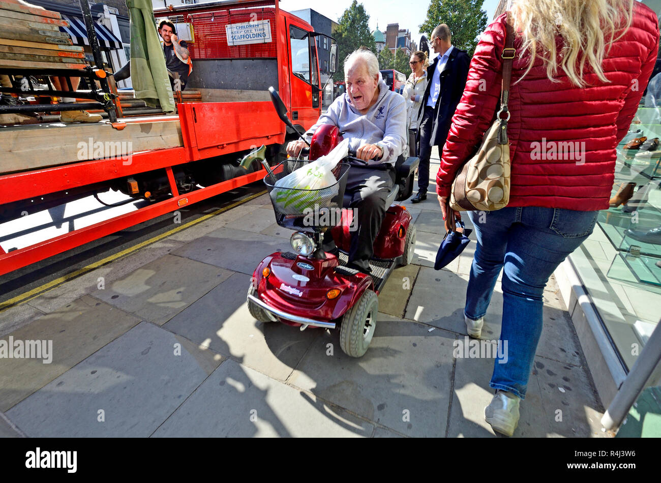Homme conduisant un scooter de mobilité sur la chaussée dans le centre de Londres, Angleterre, Royaume-Uni. Banque D'Images
