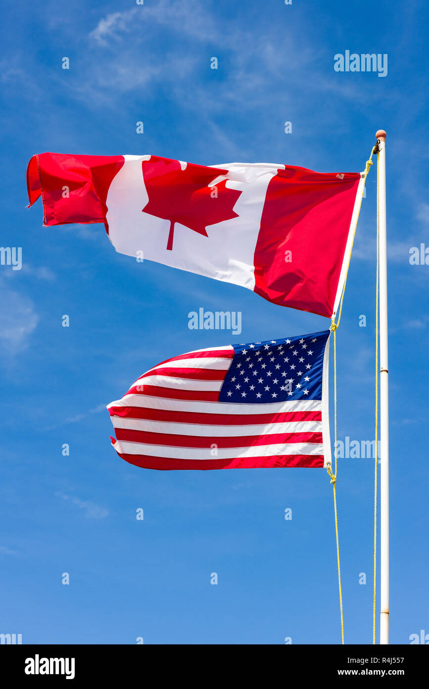 Grand drapeau canadien au-dessus de petits drapeau américain sur un poteau blanc dans le vent contre un ciel bleu Banque D'Images