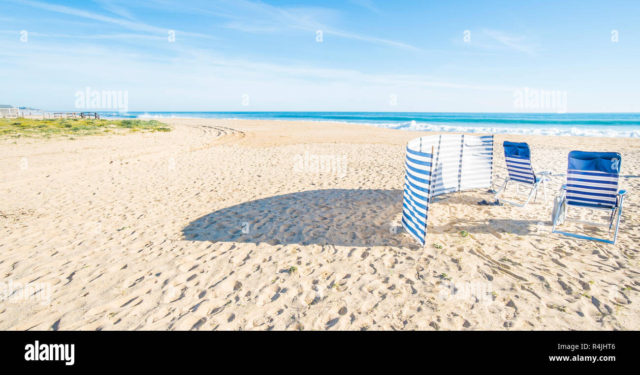 Chaises bleu et blanc et à l'abri du vent plage déserte Banque D'Images
