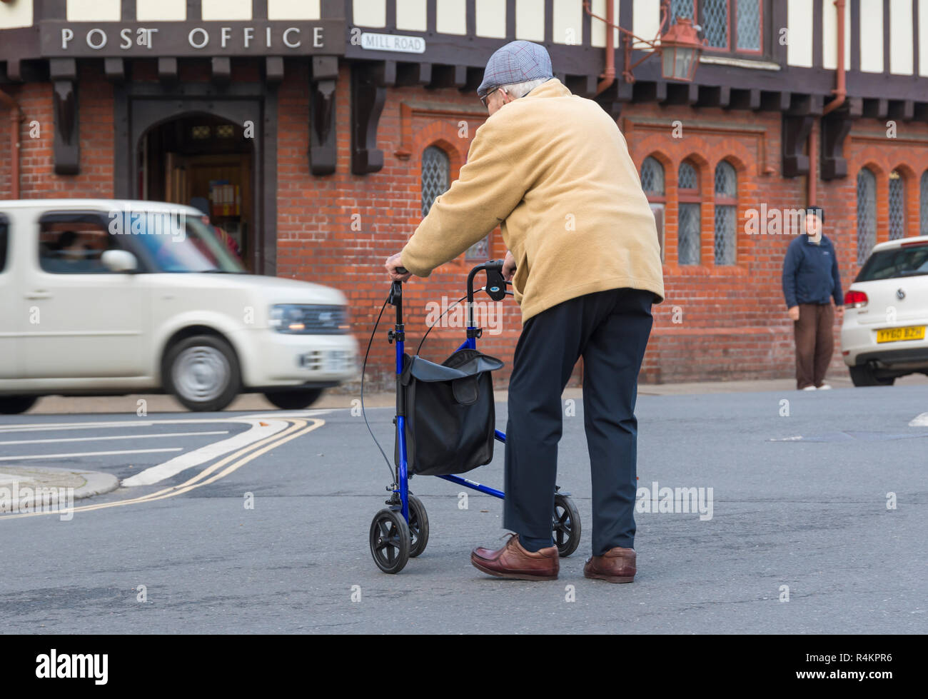 Vieil homme marchant sur une route assistée par un 3 roues Walker au Royaume-Uni. Personne Senior shopping avec Déambulateur à roues. Banque D'Images