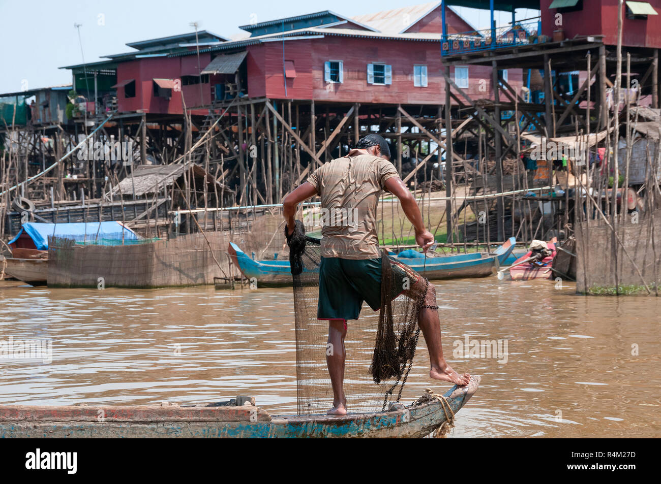 Pêcheur en face de maisons de village de pêcheurs sur pilotis, dans la saison sèche, situé sur les rives d'un estuaire de le brancher sur le lac Tonle Sap, Cambodge Banque D'Images