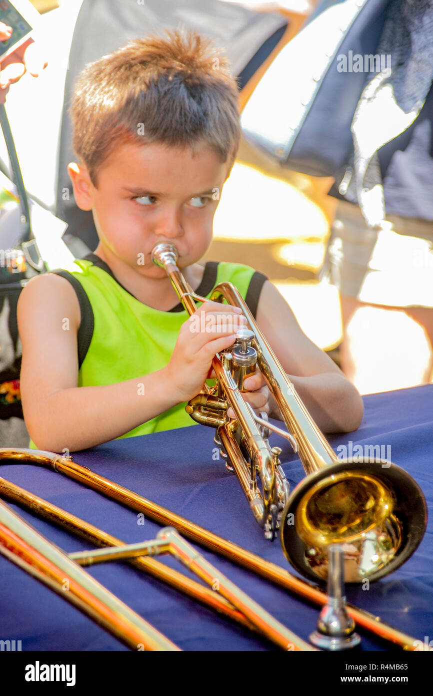 Un dix-année-vieux garçon renflement les joues alors qu'il tente de jouer la trompette d'un musicien lors d'une pause à un festival de musique en plein air à Costa Mesa, CA. Banque D'Images