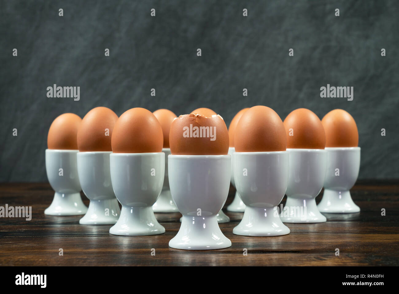 Dix œufs durs dans white egg cups sur une table en bois dans un triangle avant l'arrangement est d'oeufs cassées Banque D'Images