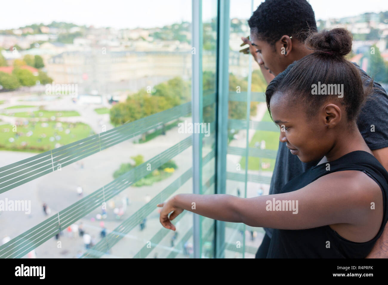 Jeune femme faisant tout en regardant par la fenêtre avec son petit ami dans un bâtiment moderne Banque D'Images