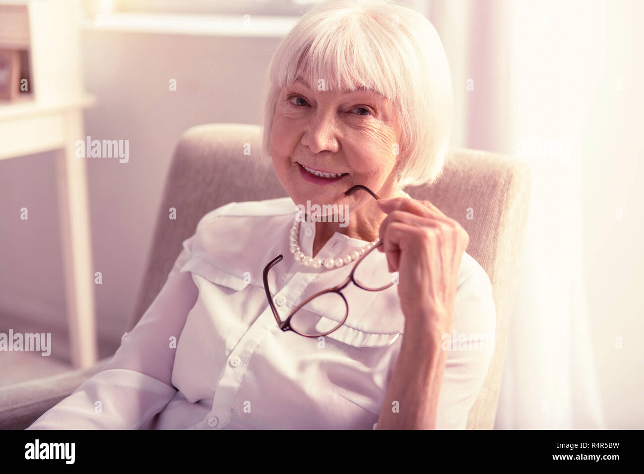 Smiling white-haired woman holding glasses with hand Banque D'Images