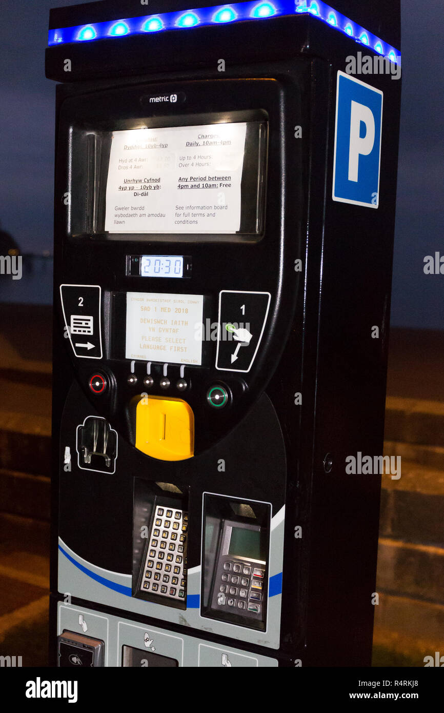 Parking meter moderne et restrictions panneau indiquant en gallois et en anglais. Llandudno front nord du Pays de Galles UK la nuit. Banque D'Images