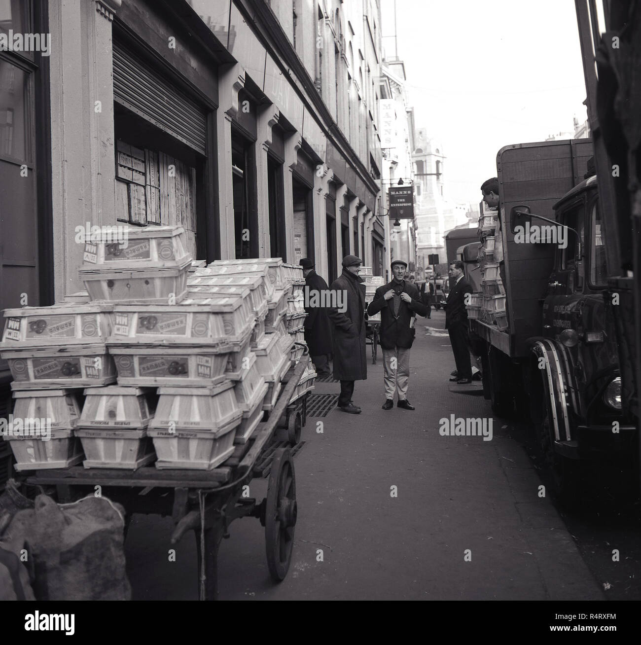 Années 1960, historique, les hommes sur un trottoir de parler par un camion garé sur le trottoir et d'un panier rempli de caisses, à Covent Garden, Londres, le site des fruits frais wholelsale et marché aux fleurs à cette époque. Banque D'Images