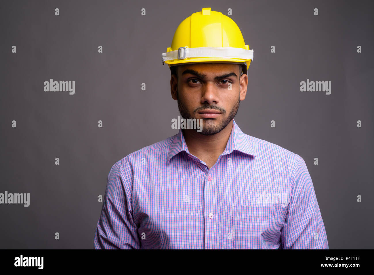 Beau jeune homme d'affaires indien wearing hardhat contre gray b Banque D'Images