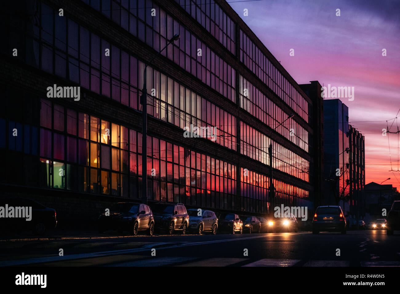 Bâtiment en verre avec ville en soirée et vibrant violet, orange et rouge Ciel de coucher du soleil à elle et les voitures dans la rue, Minsk, Biélorussie Banque D'Images