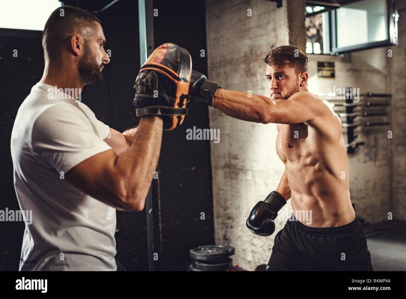 Jeune homme musclé est la pratique de l'exercice dans la salle de sport boxe l'appui de son entraîneur personnel. Banque D'Images