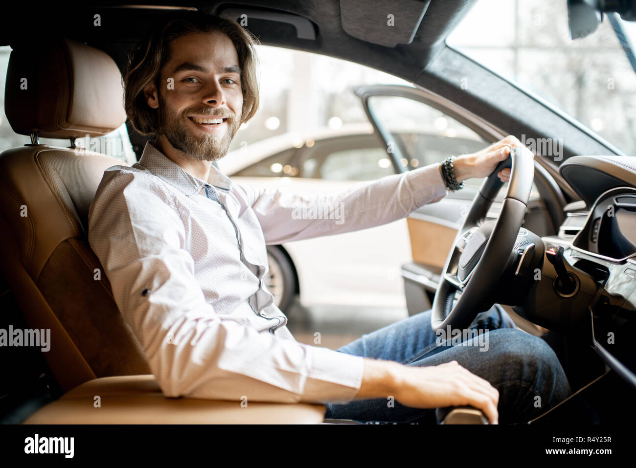 Portrait d'un jeune homme séduisant d'essayer une nouvelle voiture assis dans la voiture de luxe à l'intérieur de la salle d'exposition Banque D'Images