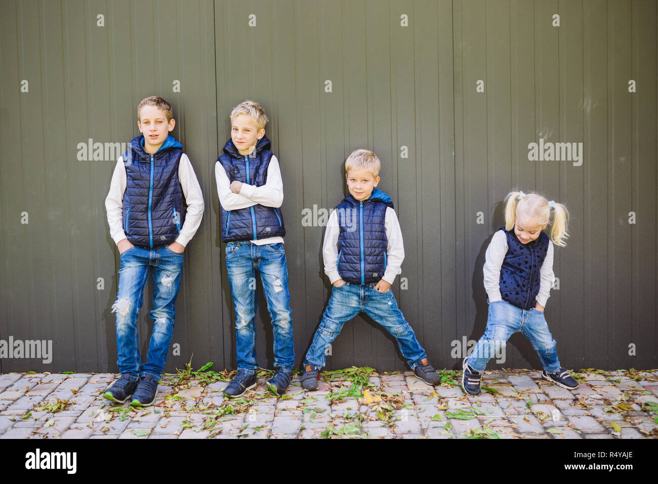 Funny Portrait grande famille de trois frères et sœur posant debout sur fond de croissance de mur en pleine croissance. Tout aussi élégamment vêtus de gilets et bleu jeans. Thème fille en cercle masculin Banque D'Images