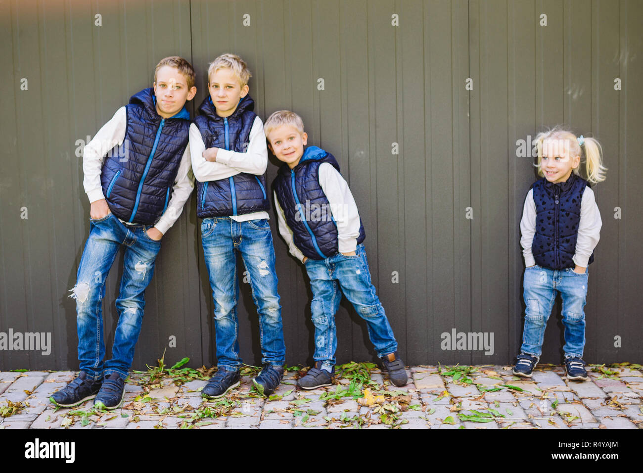 Funny Portrait grande famille de trois frères et sœur posant debout sur fond de croissance de mur en pleine croissance. Tout aussi élégamment vêtus de gilets et bleu jeans. Thème fille en cercle masculin Banque D'Images