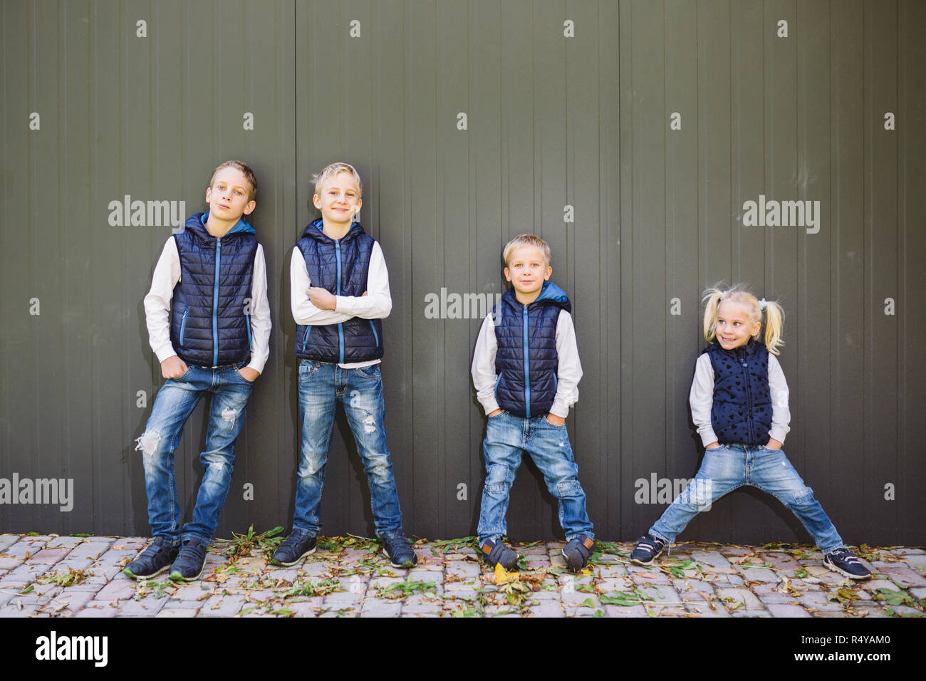 Funny Portrait grande famille de trois frères et sœur posant debout sur fond de croissance de mur en pleine croissance. Tout aussi élégamment vêtus de gilets et bleu jeans. Thème fille en cercle masculin Banque D'Images
