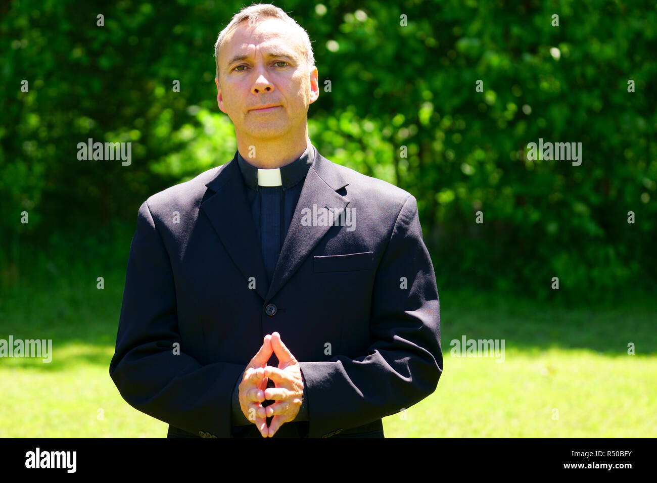 Un bon prêtre catholique est debout dans le jardin, nous regarder sérieusement. Banque D'Images