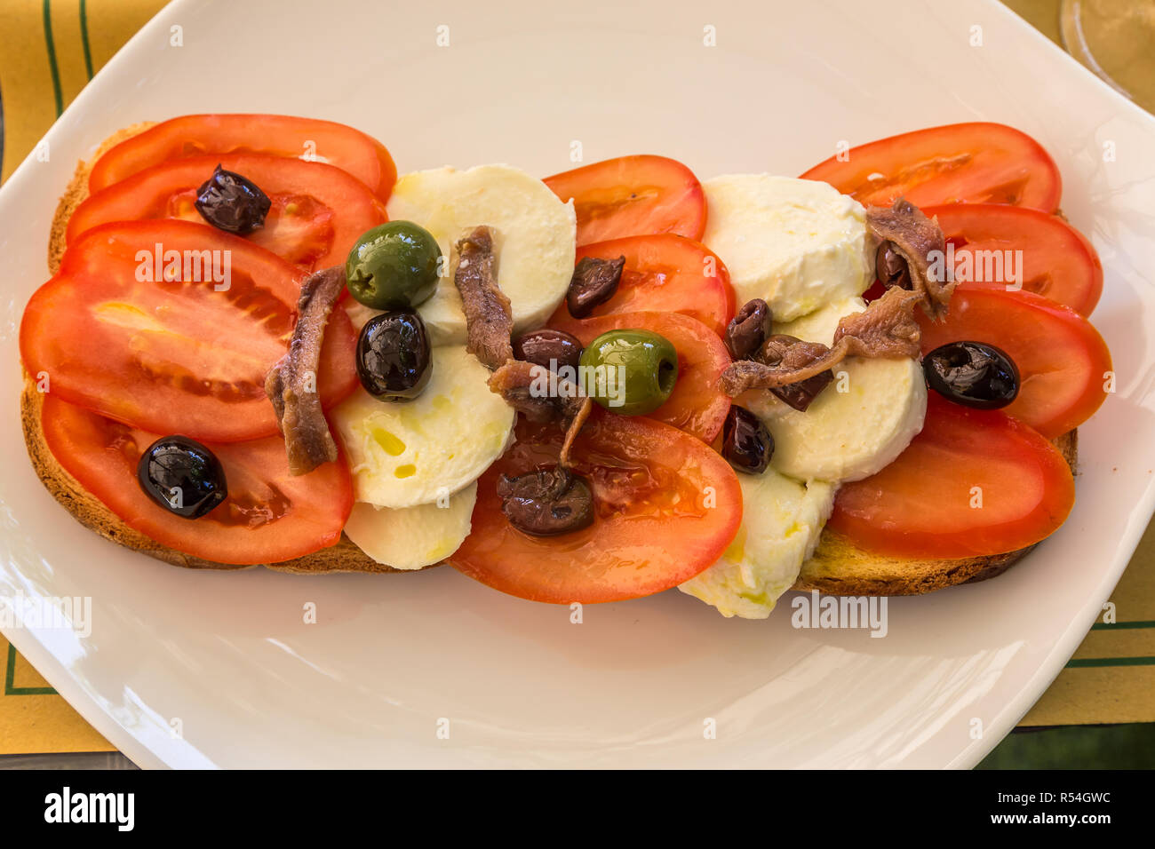 Collation au déjeuner de tomates, olives et fromage. anchois sur du pain, servi sur une plaque blanche. Banque D'Images