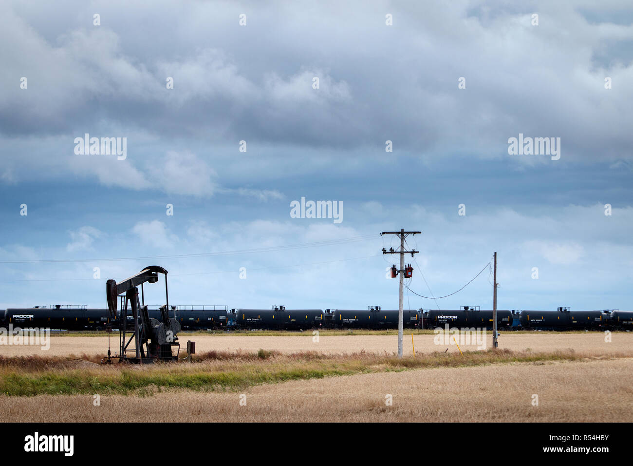 Un vérin à pompe pompe aspire l'huile d'un puits d'huile de schiste en dehors de Williston, une section du champ de pétrole de Bakken. En arrière-plan, un train de marchandises avec des wagons-citernes pleins de pétrole. Banque D'Images