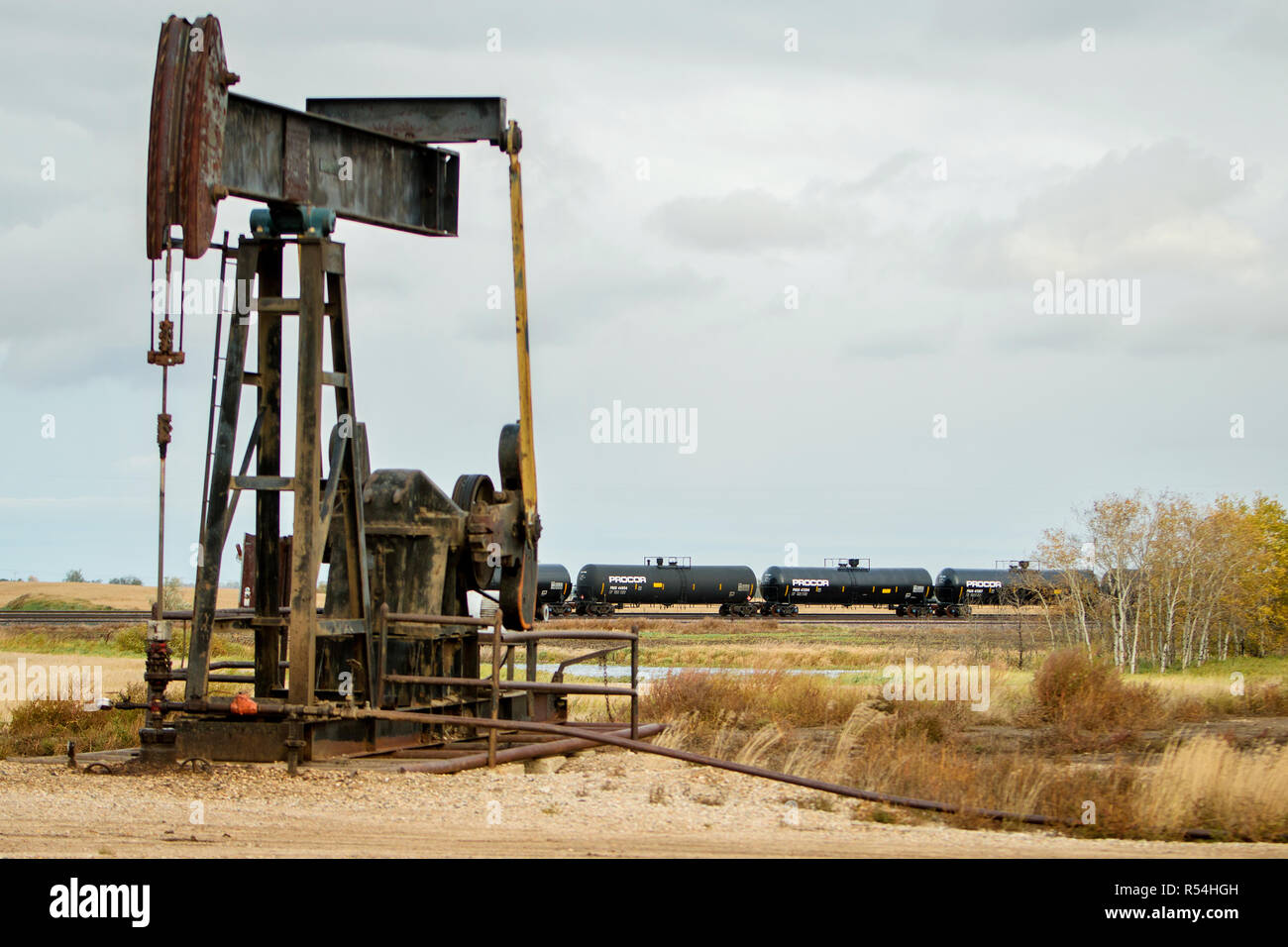 Un vérin à pompe pompe aspire l'huile d'un puits d'huile de schiste en dehors de Williston, une section du champ de pétrole de Bakken. En arrière-plan, un train de marchandises avec des wagons-citernes pleins de pétrole. Banque D'Images