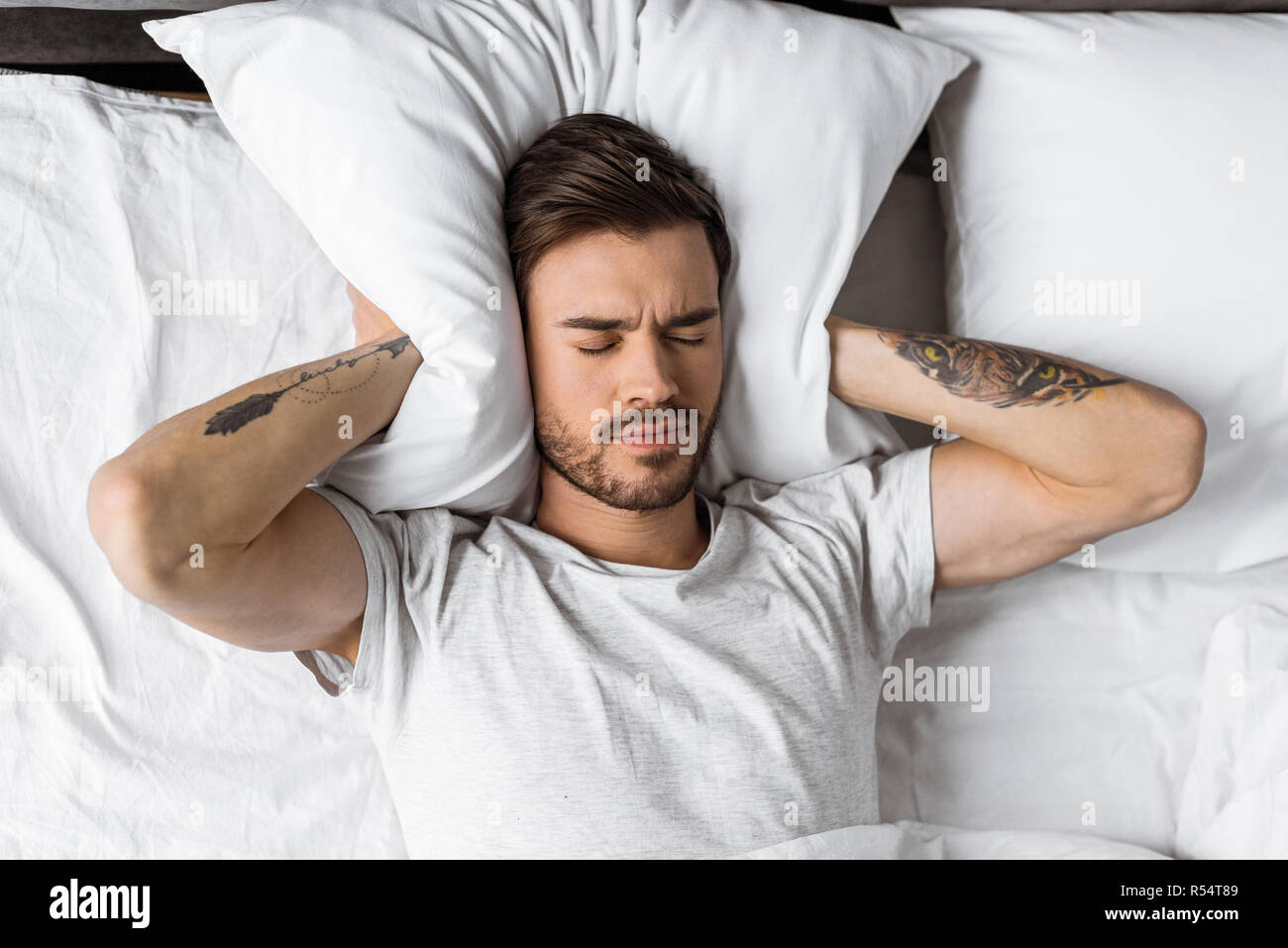 Jeune homme de fermer les oreilles avec oreiller au lit le matin Banque D'Images