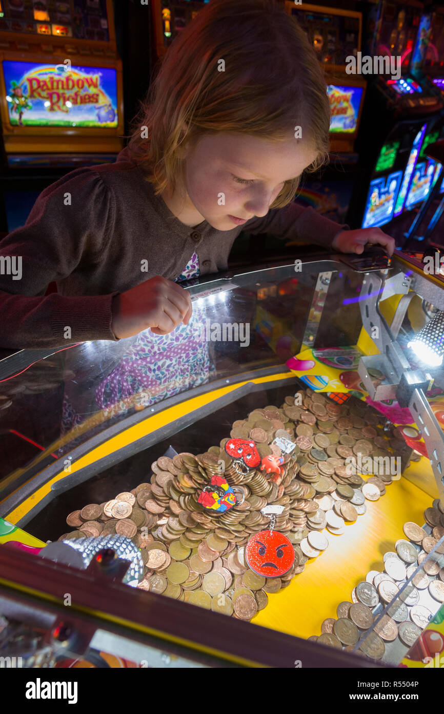 Jeune fille âgée de huit ans, l'âge de 8 ans de jouer sur un coin pusher traditionnels populaires / pièces poussant en jeu pier arcade fun house. UK. (98). Banque D'Images