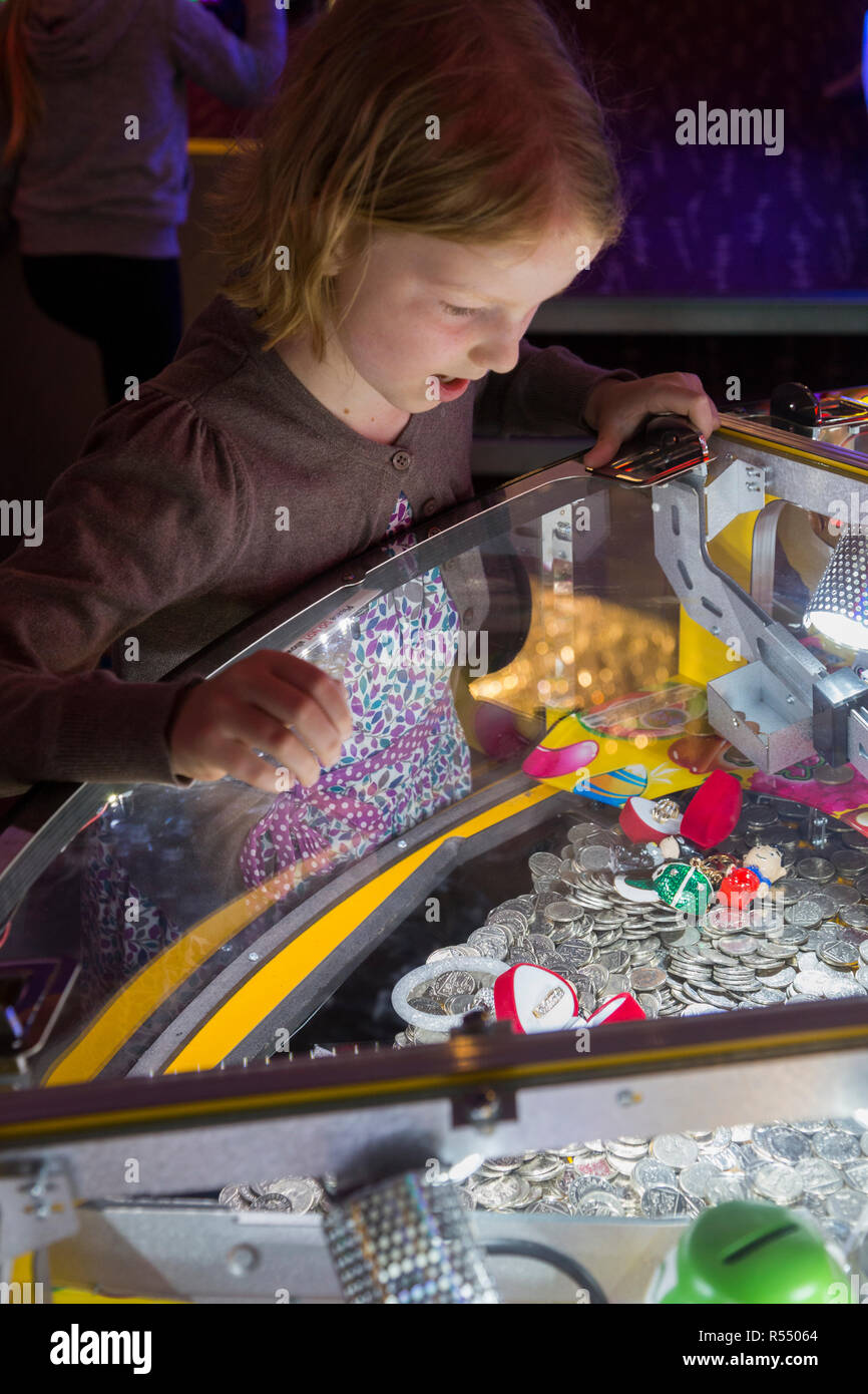 Jeune fille âgée de huit ans, l'âge de 8 ans de jouer sur un coin pusher traditionnels populaires / pièces poussant en jeu pier arcade fun house. UK. (98). Banque D'Images