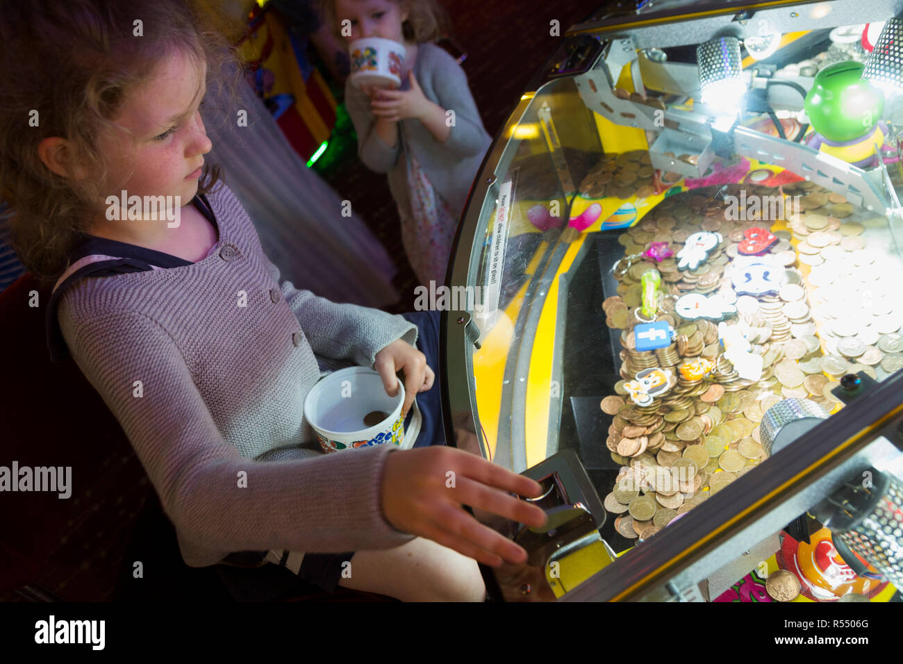 Jeune fille âgée de 6 ans / 6 ans jouant sur un coin pusher traditionnels populaires / pièces poussant en jeu pier arcade fun house. UK. (98). Banque D'Images