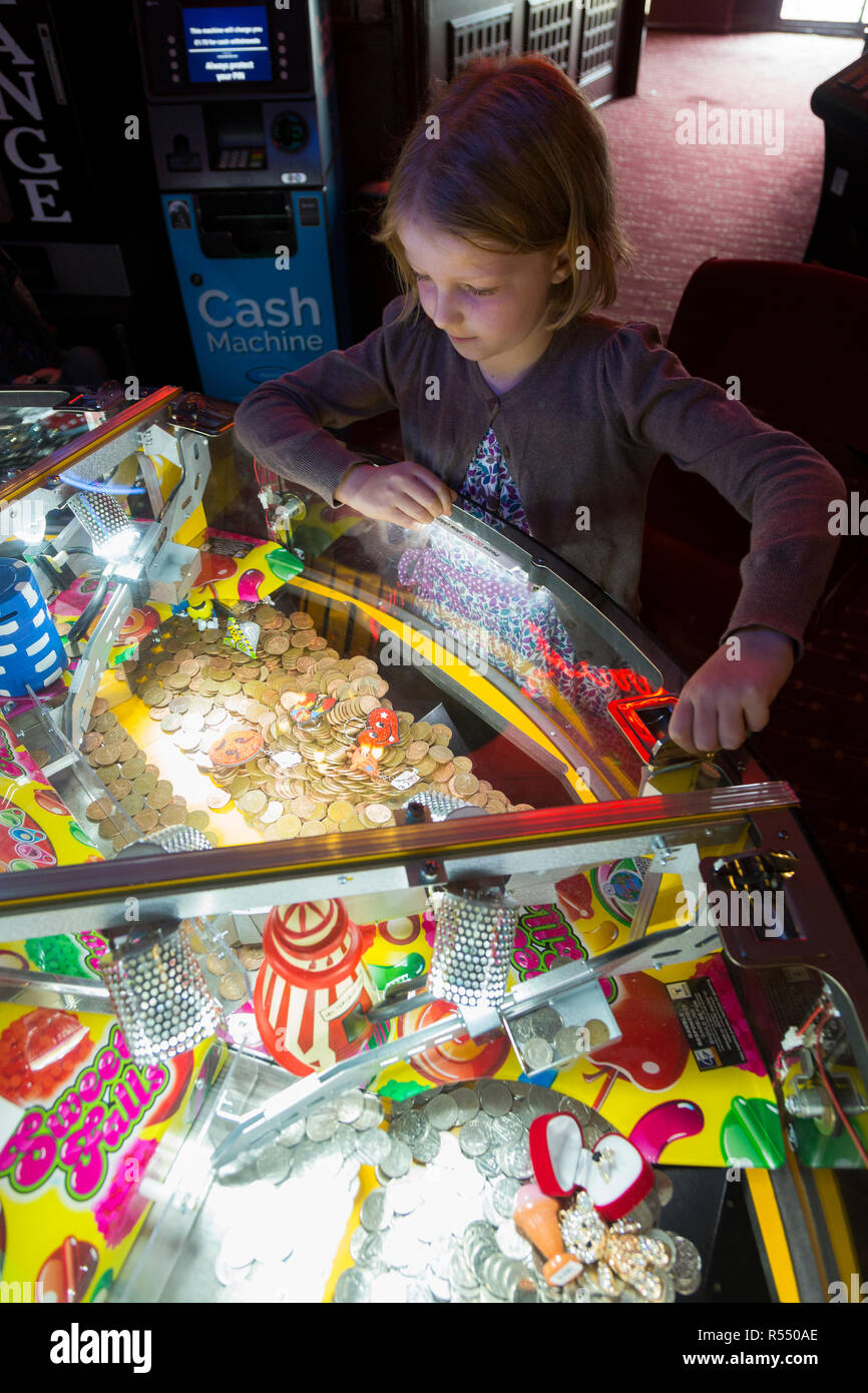 Jeune fille âgée de huit ans, l'âge de 8 ans de jouer sur un coin pusher traditionnels populaires / pièces poussant en jeu pier arcade fun house. UK. (98). Banque D'Images