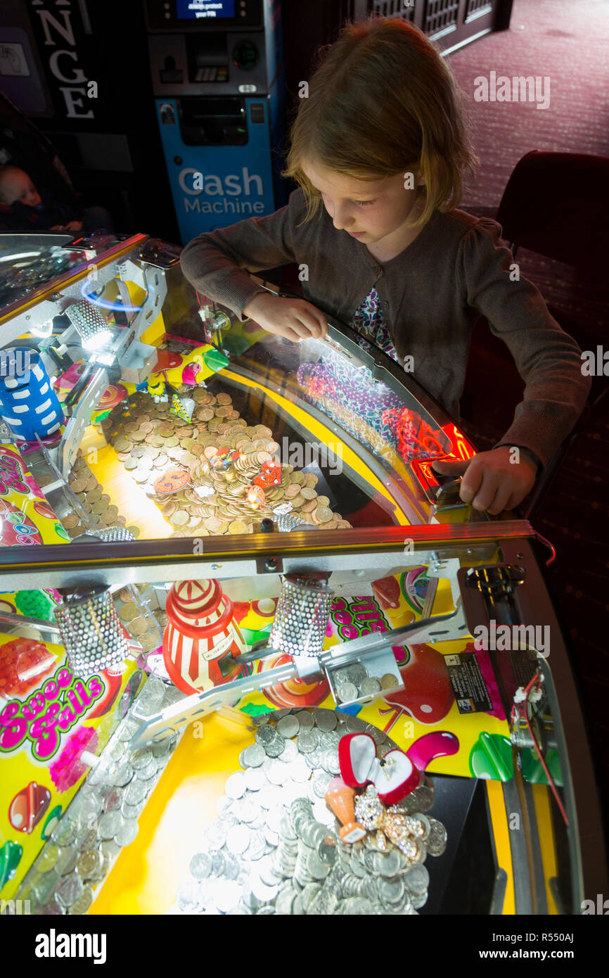 Jeune fille âgée de huit ans, l'âge de 8 ans de jouer sur un coin pusher traditionnels populaires / pièces poussant en jeu pier arcade fun house. UK. (98). Banque D'Images