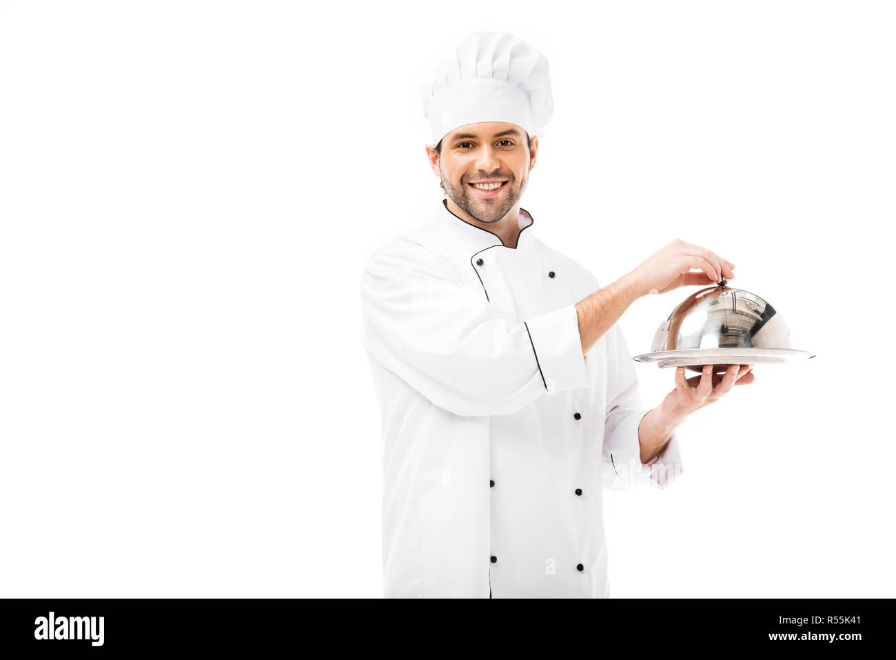 Beau jeune chef holding plat de service avec dome et looking at camera isolated on white Banque D'Images