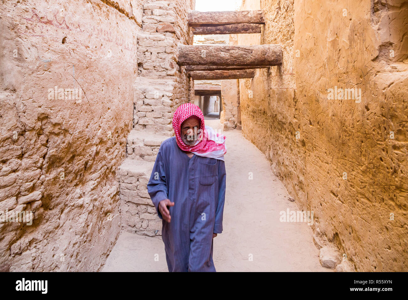 Dakhla Oasis, Egypte. Ancien égyptien arabe man walking habillé de bleu robe masculine nationale thawb, par l'intermédiaire de la rue médiévale, ville ancienne à Al Qasr. Banque D'Images